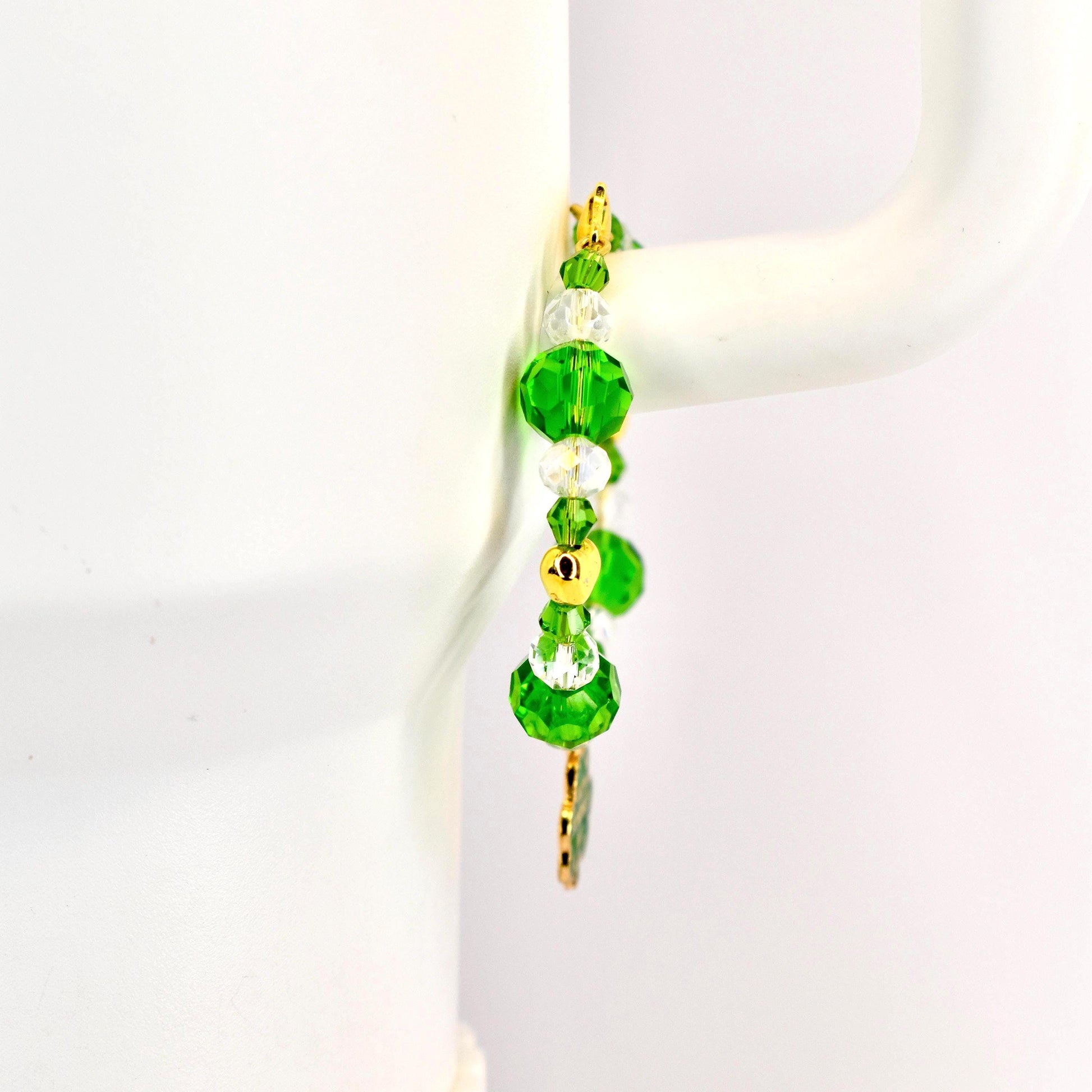 A beaded bracelet with green and clear crystal beads and gold accents. The bracelet features large, faceted green beads, smaller clear beads, and gold-colored metal spacers. A gold charm hangs from the bottom.