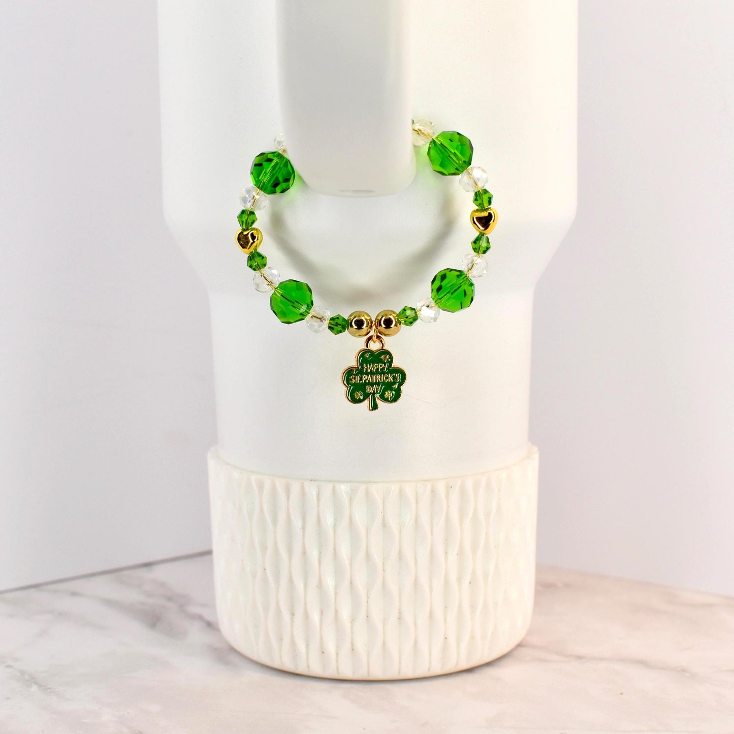 A St. Patrick's Day handle bracelet with green and clear beads, gold accents, and a shamrock charm. The charm has the words "Happy St. Patrick's Day" on it. The bracelet is on a white background.