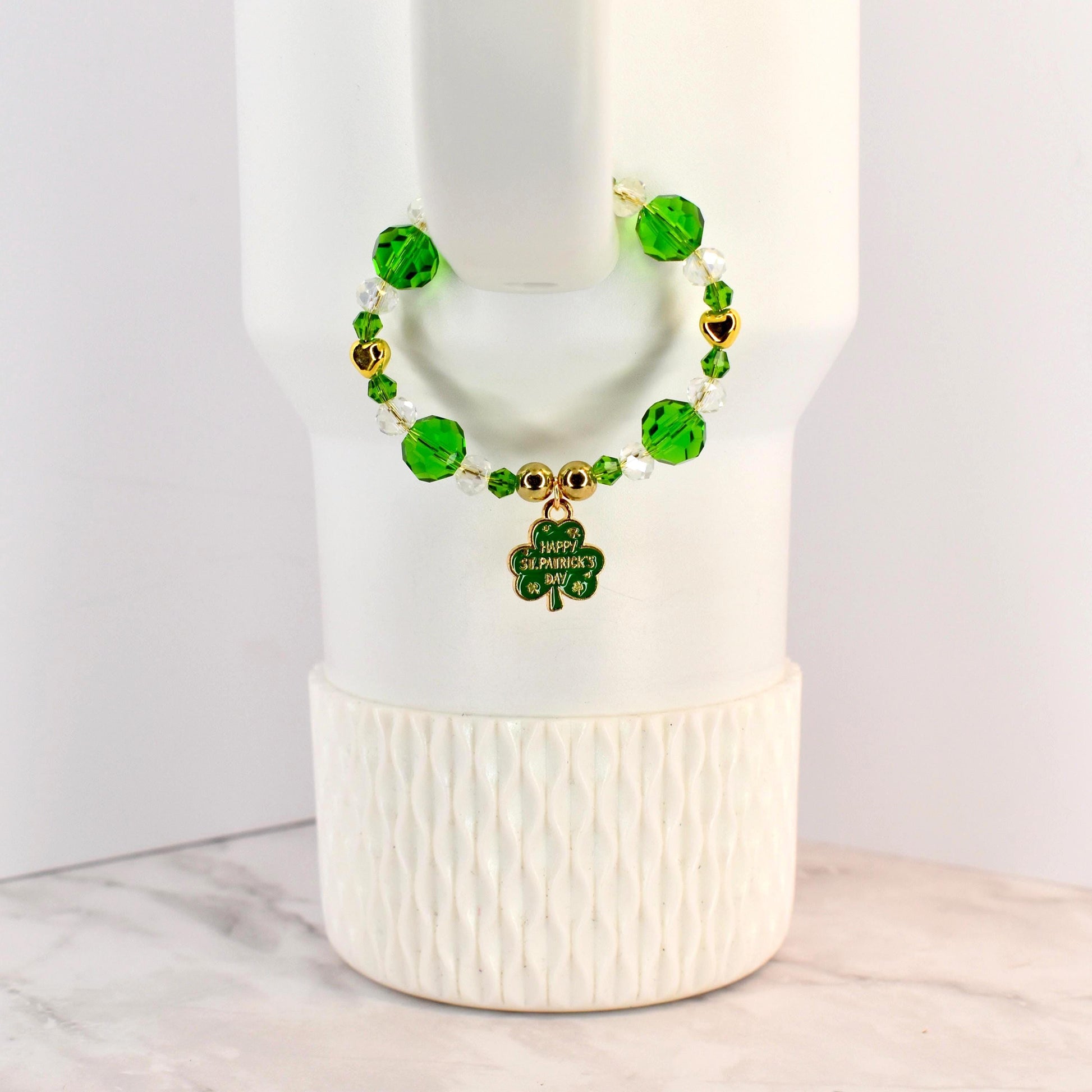 A St. Patrick's Day handle bracelet with green and clear beads, gold accents, and a shamrock charm. The charm has the words "Happy St. Patrick's Day" on it. The bracelet is on a white background.