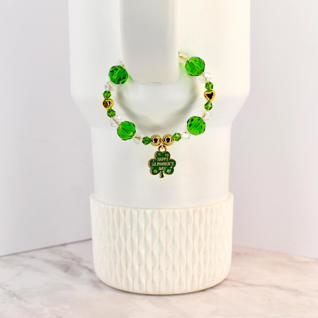 A St. Patrick's Day handle bracelet with green and clear beads, gold accents, and a shamrock charm. The charm has the words "Happy St. Patrick's Day" on it. The bracelet is on a white background.