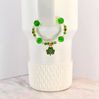 A St. Patrick's Day handle bracelet with green and clear beads, gold accents, and a shamrock charm. The charm has the words "Happy St. Patrick's Day" on it. The bracelet is on a white background.