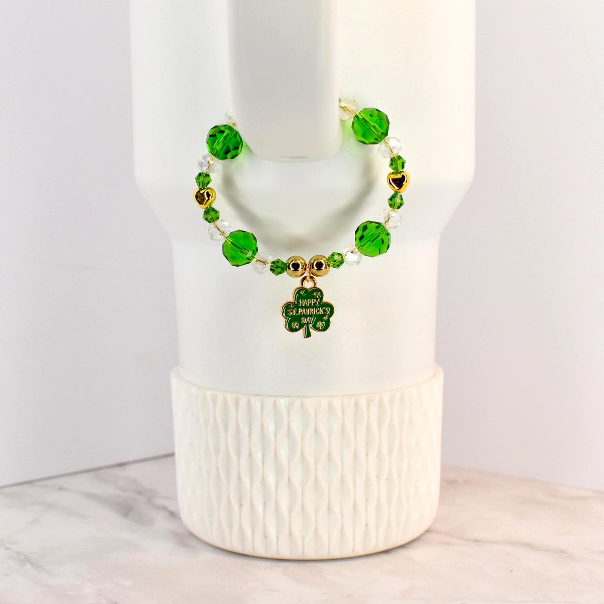 A St. Patrick's Day handle bracelet with green and clear beads, gold accents, and a shamrock charm. The charm has the words "Happy St. Patrick's Day" on it. The bracelet is on a white background.