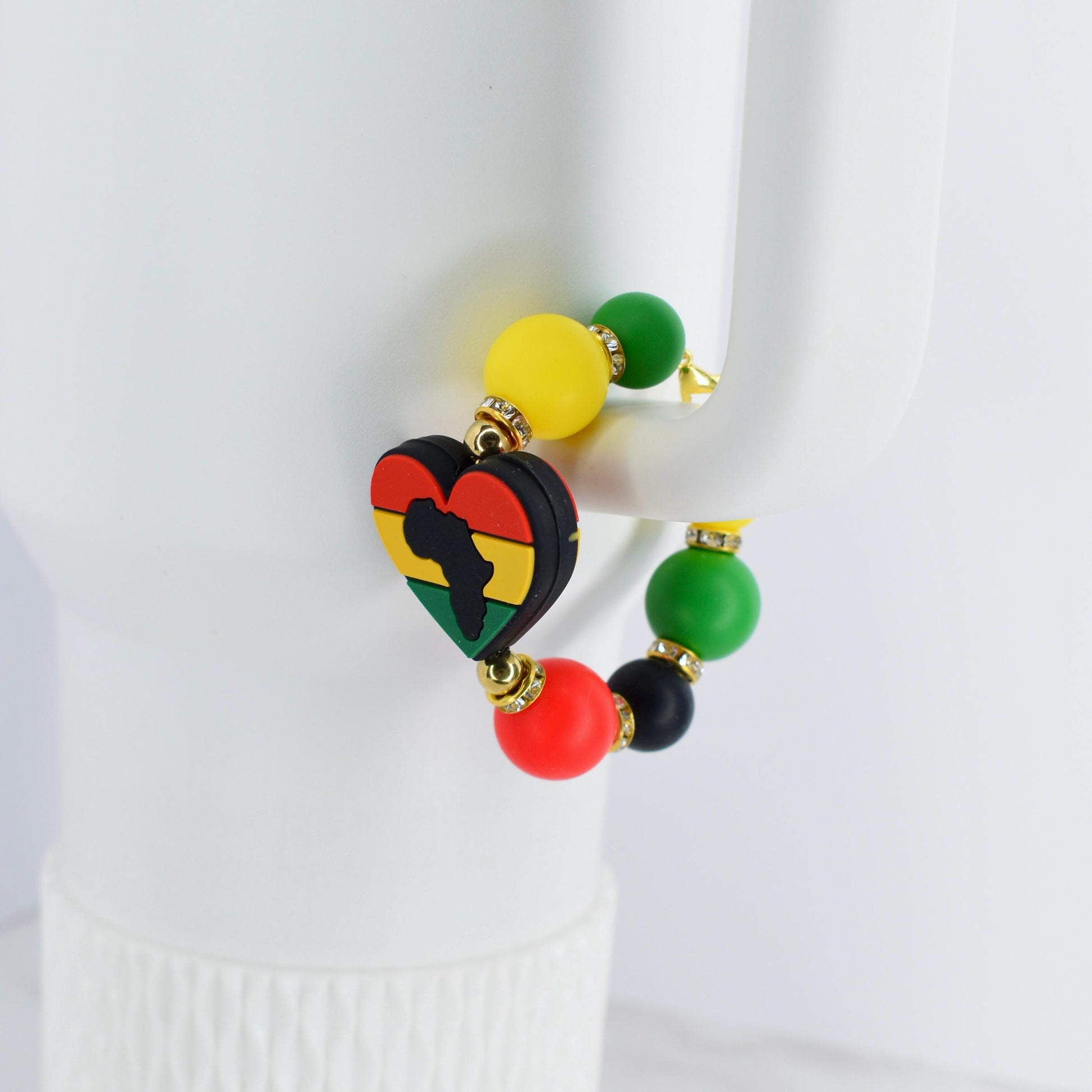 A beaded bracelet featuring a heart-shaped charm with the African continent in black, yellow, red, and green. The bracelet includes yellow, green, red, and black beads. The bracelet is accented with gold-colored metal.