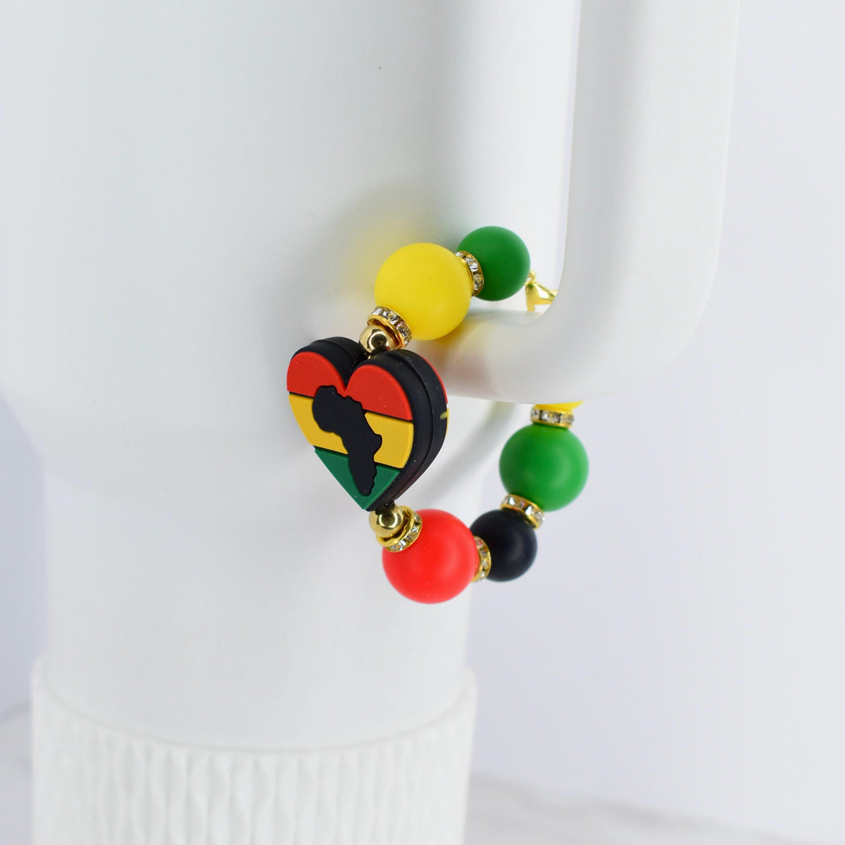A beaded bracelet featuring a heart-shaped charm with the African continent in black, yellow, red, and green. The bracelet includes yellow, green, red, and black beads. The bracelet is accented with gold-colored metal.