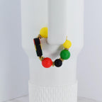 A beaded bracelet with yellow, green, red, and black beads. The bracelet has gold-colored accents and a black bead with a colorful design. The bracelet is displayed on a white background.