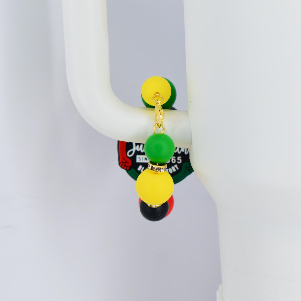 A Stanley handle bracelet featuring a gold-colored chain and colorful beads. The bracelet has yellow, green, black, and red beads. The bracelet is attached to a white surface. The bracelet has a tag with text.