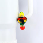 A colorful handle bracelet featuring a heart-shaped pendant with the outline of Africa in black. The heart is colored in red, yellow, and green, with yellow and green beads above and a red bead below. The bracelet is attached to a white object.