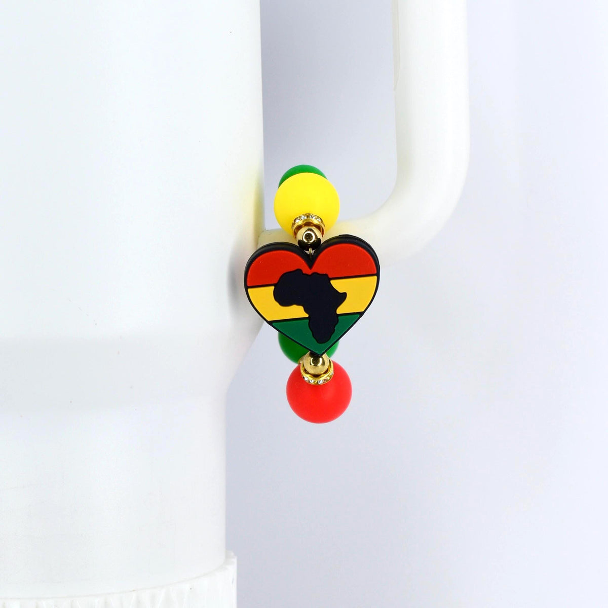 A colorful handle bracelet featuring a heart-shaped pendant with the outline of Africa in black. The heart is colored in red, yellow, and green, with yellow and green beads above and a red bead below. The bracelet is attached to a white object.