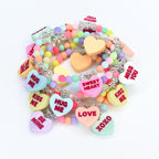 A collection of colorful beaded bracelets with heart-shaped charms. The charms feature phrases like "Kiss Me," "Hug Me," and "Sweet Heart" in red lettering. The bracelets are in various pastel colors, including pink, blue, yellow, and green.