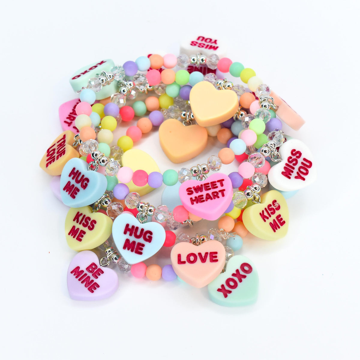 A collection of colorful beaded bracelets with heart-shaped charms. The charms feature phrases like "Kiss Me," "Hug Me," and "Sweet Heart" in red lettering. The bracelets are in various pastel colors, including pink, blue, yellow, and green.