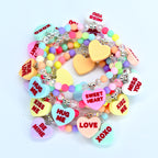 A collection of colorful beaded bracelets with heart-shaped charms. The charms feature phrases like "Kiss Me," "Hug Me," and "Sweet Heart" in red text. The beads are pastel colors, and the bracelets have silver-toned accents.