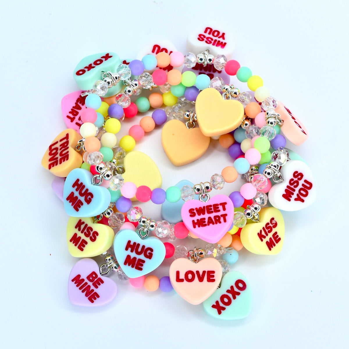 A collection of colorful beaded bracelets with heart-shaped charms. The charms feature phrases like "Kiss Me," "Hug Me," and "Sweet Heart" in red text. The beads are pastel colors, and the bracelets have silver-toned accents.