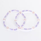 Two beaded bracelets. Each bracelet is a circle of small, light purple, clear, and pink beads. The bracelets are on a white background. The beads are strung together with a clear string.