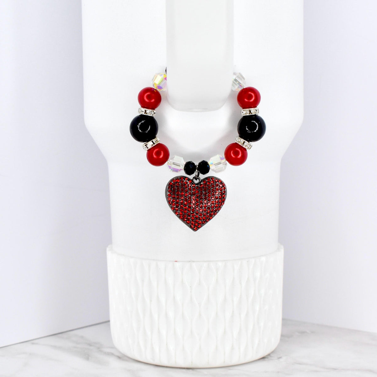 A beaded cup charm featuring red, black, and clear beads. A red heart-shaped charm with a rhinestone design hangs from the beads. The charm is designed to fit around a cup or tumbler.