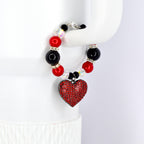 A beaded tumbler handle bracelet featuring red, black, and clear beads. A heart-shaped pendant covered in red rhinestones hangs from the bracelet. The bracelet is held up by a white surface.