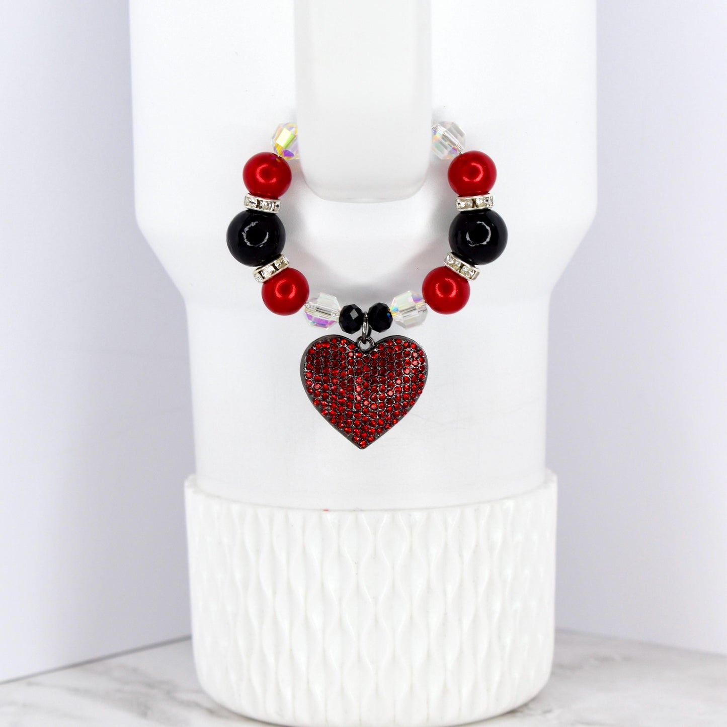 A beaded cup charm with a red heart pendant. The charm features red and black beads, clear crystal accents, and a heart-shaped pendant covered in red rhinestones. The charm is designed to fit around a cup.