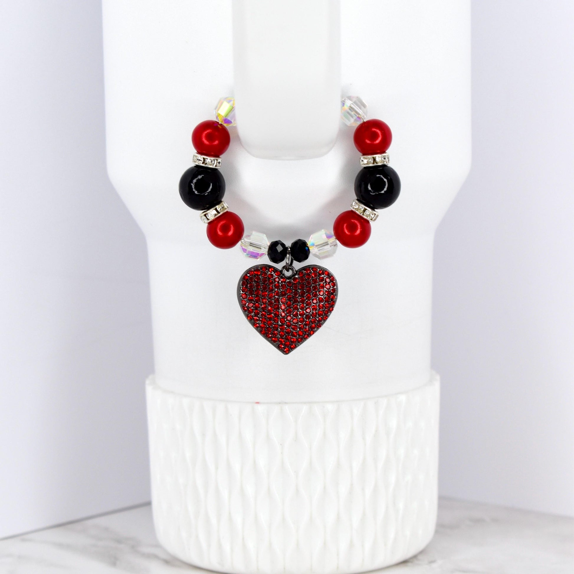 A beaded cup charm with a red heart pendant. The charm features red and black beads, clear crystal accents, and a heart-shaped pendant covered in red rhinestones. The charm is designed to fit around a cup.