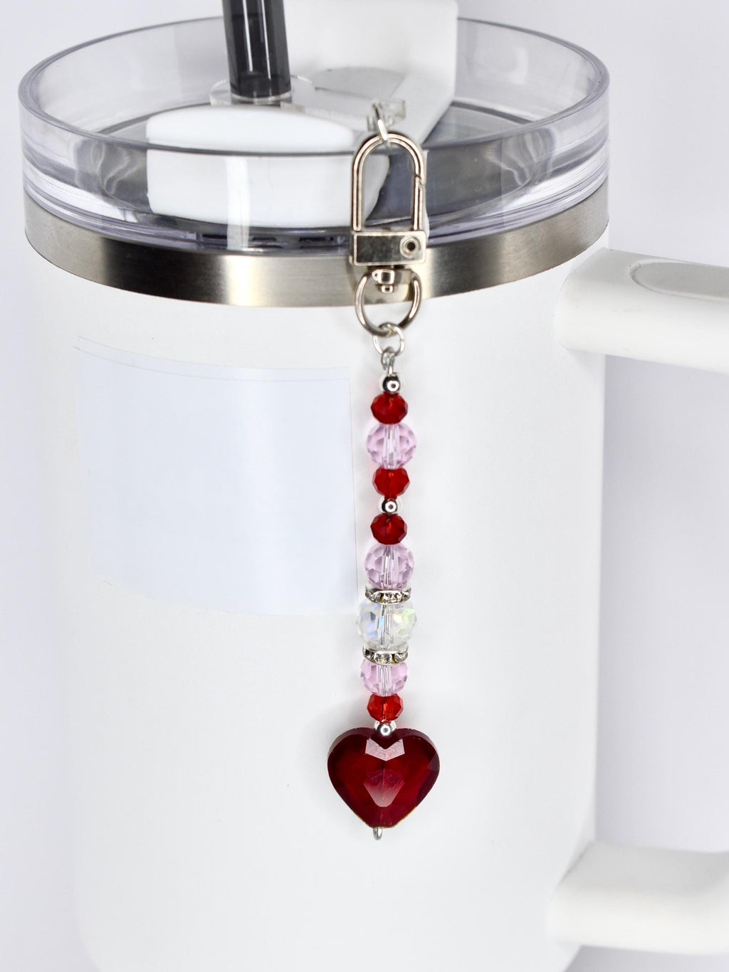 A beaded keychain with a silver clasp, featuring a strand of red, pink, and clear beads, culminating in a faceted, heart-shaped pendant. The keychain is attached to a white tumbler.