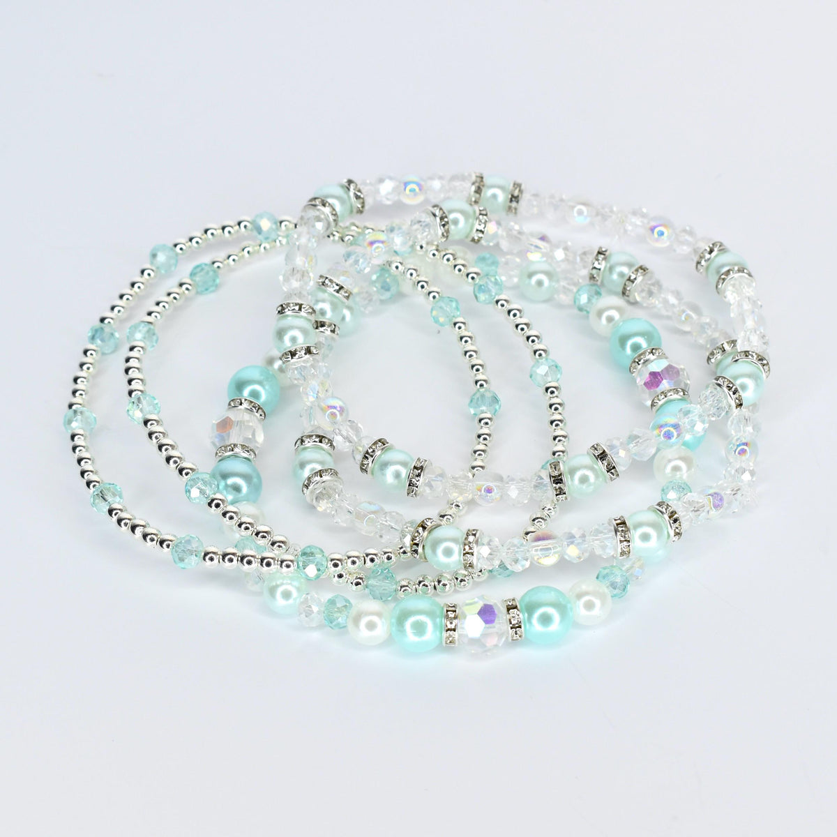 Several beaded bracelets in shades of light blue, clear, and silver. The bracelets feature a mix of beads, including round, pearl-like beads, and smaller, sparkling beads. The bracelets are arranged in a layered, intertwined fashion.