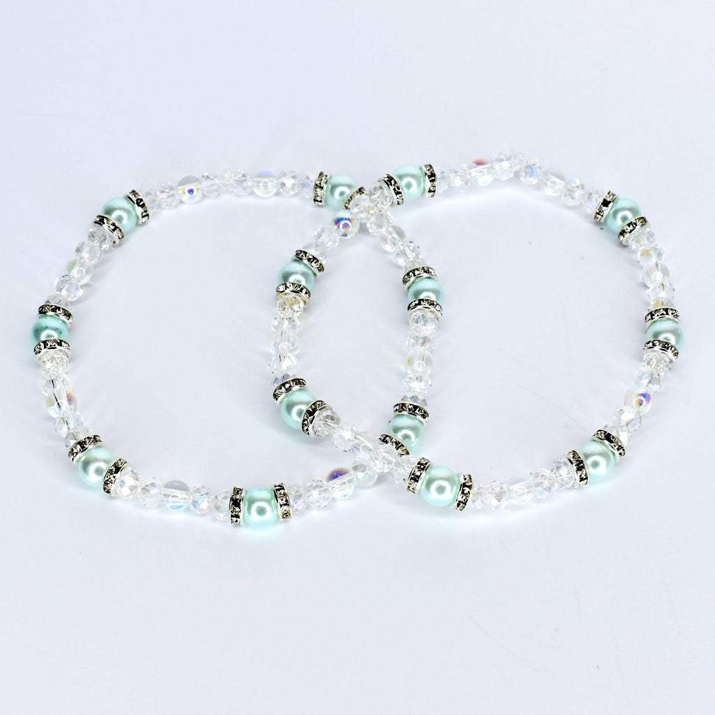 Two delicate bracelets with clear crystal beads and light blue pearl-like beads. The bracelets have silver-colored accents and are arranged in a figure-eight shape against a white background. The jewelry is likely for a special occasion.