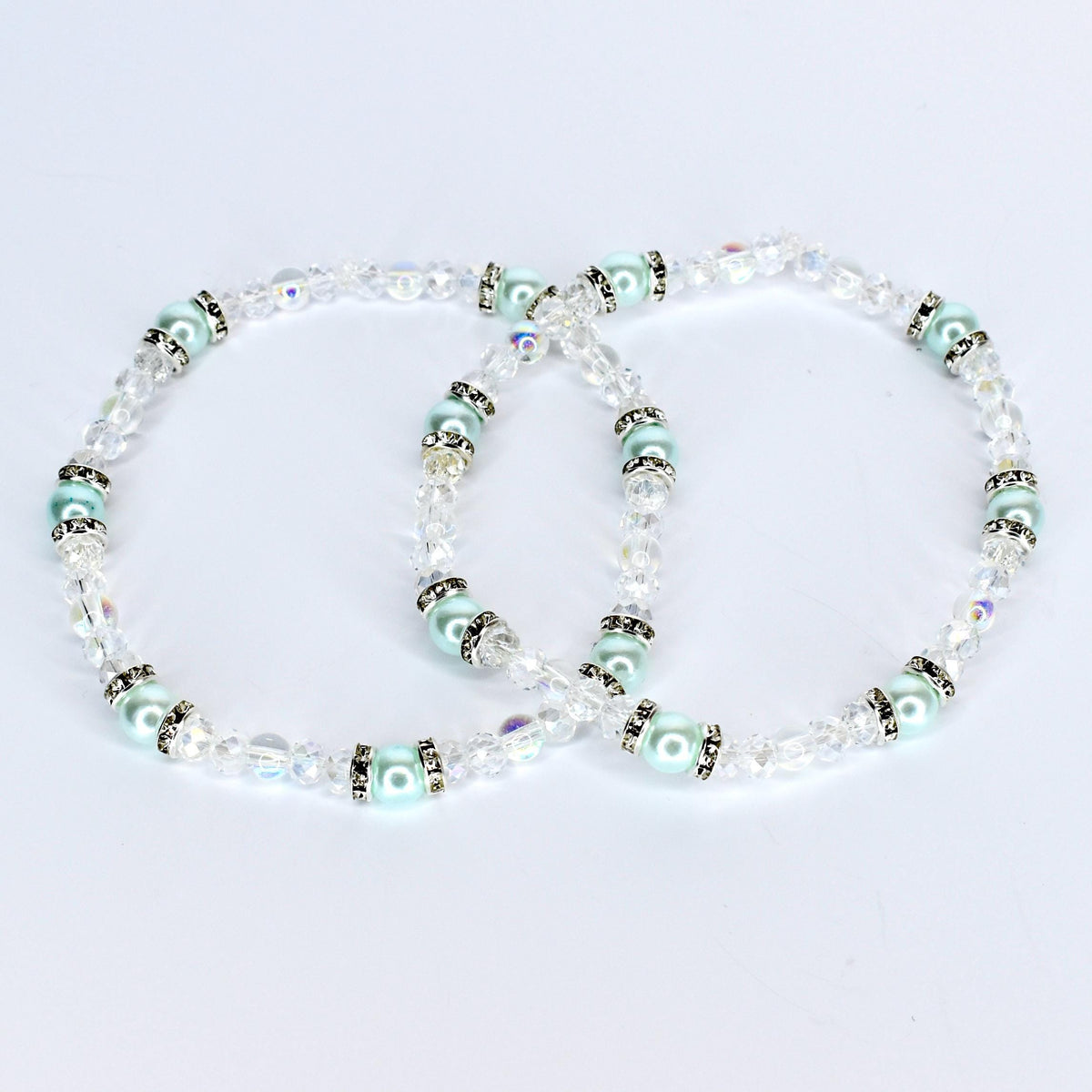 Two delicate bracelets with clear crystal beads and light blue pearl-like beads. The bracelets have silver-colored accents and are arranged in a figure-eight shape against a white background. The jewelry is likely for a special occasion.