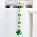 A green, crystal and gold beaded tumbler straw charm with a green shamrock charm at the bottom.