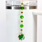 A green, crystal and gold beaded tumbler straw charm with a green shamrock charm at the bottom.