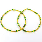 Two gold-colored anklets with green and gold-colored beads. The anklets are made of small, round gold beads and square gold beads, interspersed with green, faceted beads. The anklets are displayed on a white background.