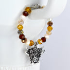 A beaded bracelet with a silver-colored charm. The bracelet features a variety of colorful beads in shades of brown and cream. The charm is a detailed depiction of a Highland cow's head.