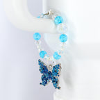 A beaded tumbler handle bracelet with a blue butterfly charm. The bracelet features light blue and clear beads. The butterfly charm is blue with silver accents and intricate detailing. The bracelet is displayed on a white surface.