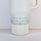 A white tumbler with three beaded bands. The bands feature light blue beads, silver accents, and a silver bow. The tumbler has a textured pattern on the bottom half.
