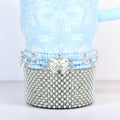 A light blue tumbler with a white floral and bow pattern. The bottom is covered in small, silver-colored faux pearls. A band of blue beads and a white bow accent the tumbler.