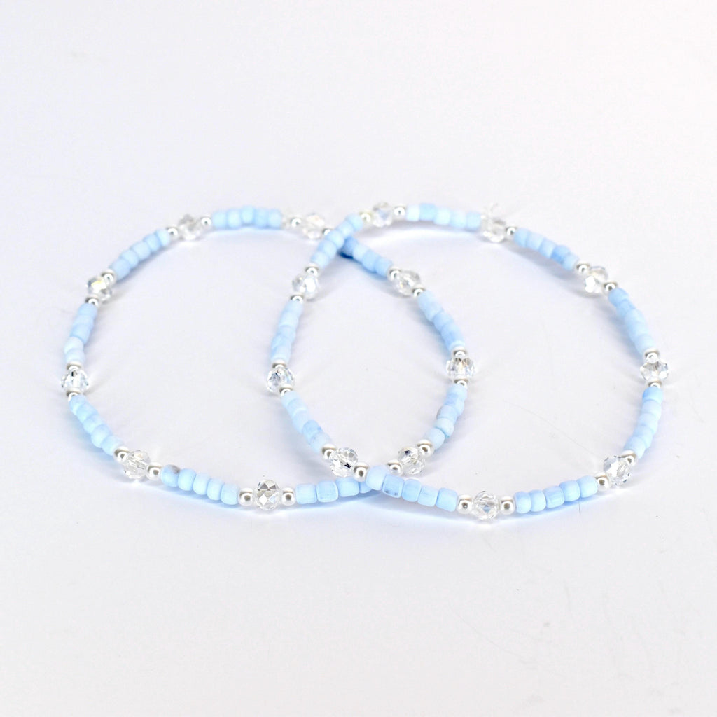 Two light blue beaded bracelets with clear crystal accents and silver-toned metal beads. The bracelets are displayed on a white background. The bracelets are delicate and elegant.