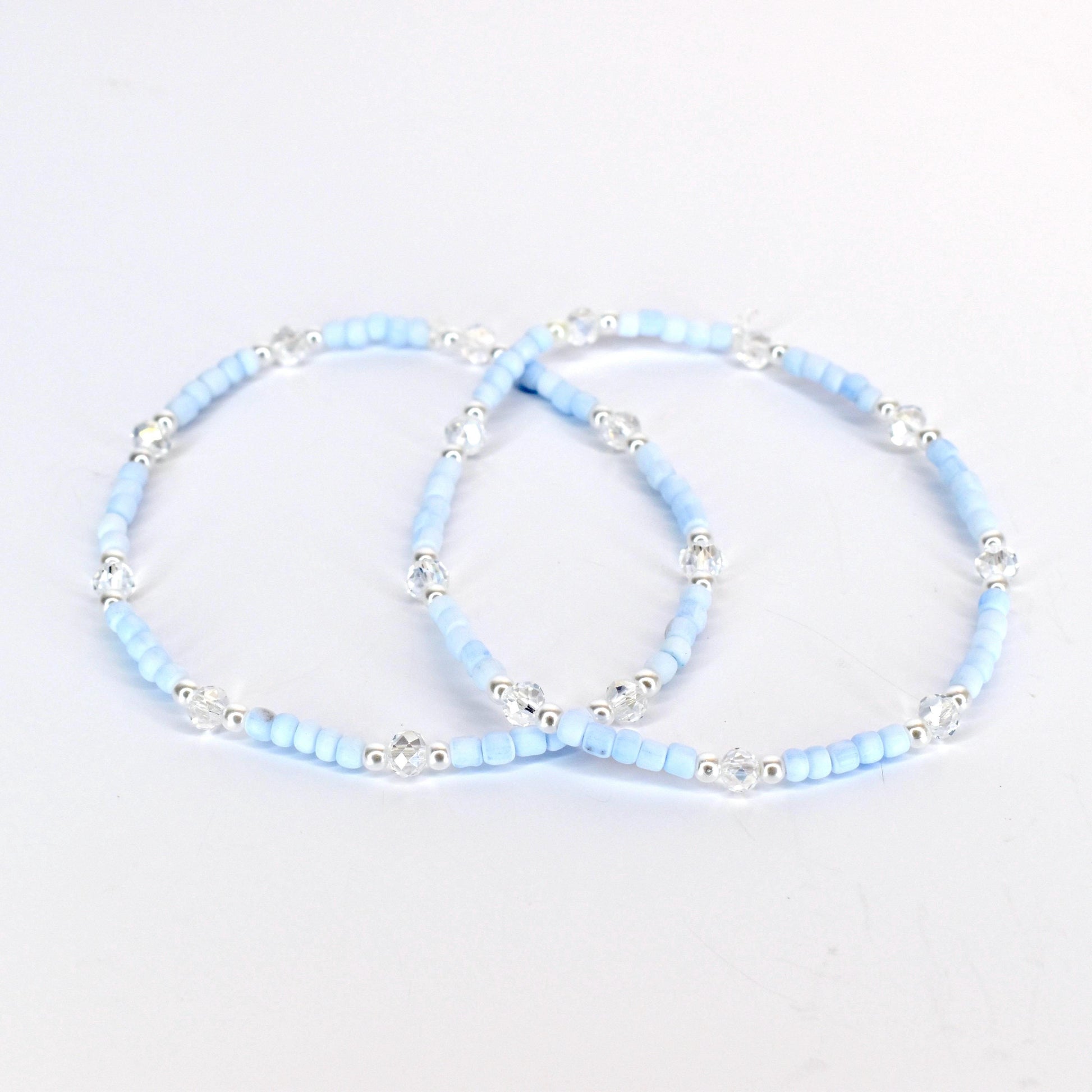 Two light blue beaded bracelets with clear crystal accents and silver-toned metal beads. The bracelets are displayed on a white background. The bracelets are delicate and elegant.