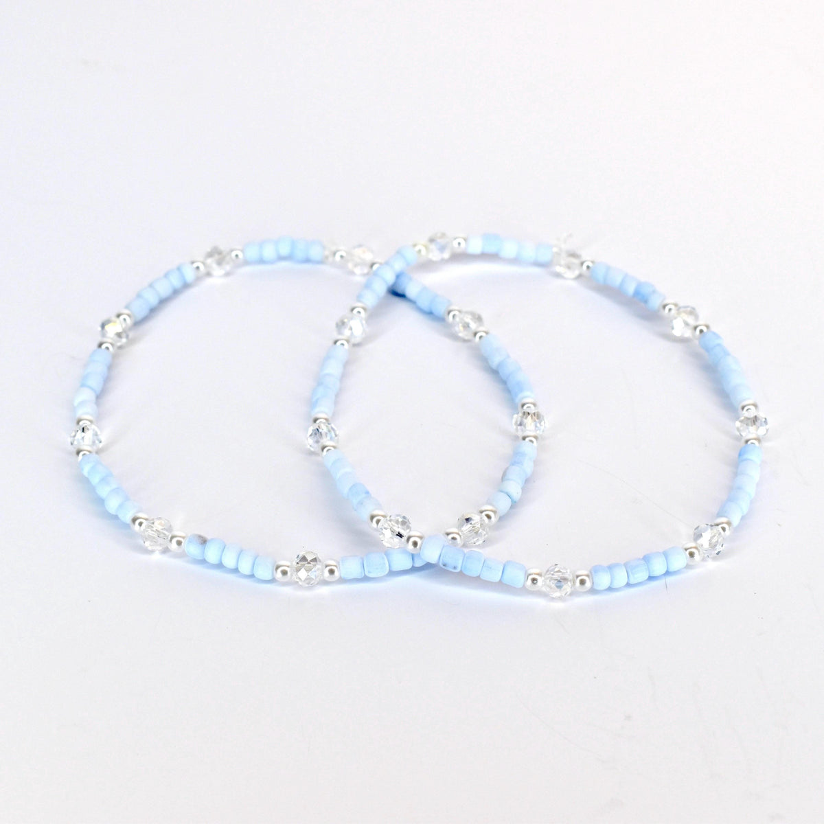 Two light blue beaded bracelets with clear crystal accents and silver-toned metal beads. The bracelets are displayed on a white background. The bracelets are delicate and elegant.