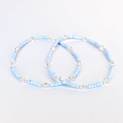 Two light blue beaded bracelets with clear crystal accents and silver-toned metal beads. The bracelets are displayed on a white background. The bracelets are delicate and elegant.