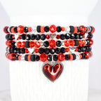 Stack of beaded bracelets in red, black, and clear crystal beads. Each bracelet features a mix of faceted and round beads, with silver heart charms. A red heart pendant with a silver border hangs from the bottom bracelet.