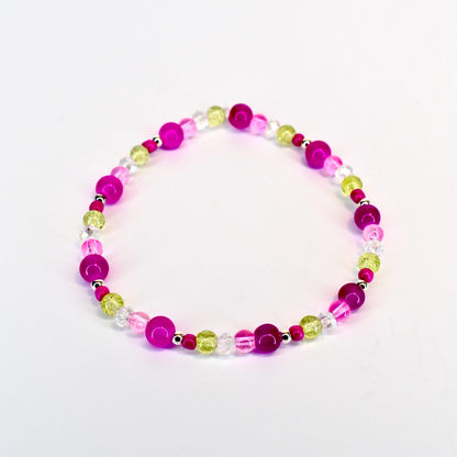 A beaded bracelet featuring a mix of vibrant colors. The bracelet includes large, round magenta beads, interspersed with smaller, clear, and light green beads. The beads are strung together with a silver-colored string, creating a colorful accessory.