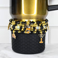 a black honey Stanley tumbler with a set of five black and gold bracelets around the base. the bracelets have new years themed charms from two of the bracelets.