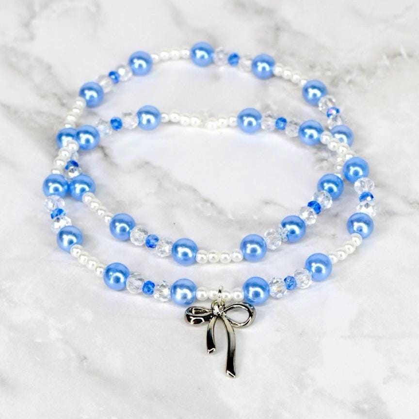 Two strands of blue and white beaded bracelets with a silver bow pendant. The beads are a mix of round and faceted shapes. The background is a white marble surface.