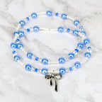 Two strands of blue and white beaded bracelets with a silver bow pendant. The beads are a mix of round and faceted shapes. The background is a white marble surface.