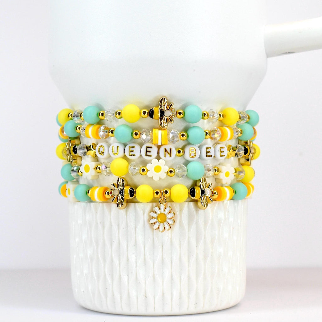 A set of five yellow and mint beaded bracelets with a daisy charm and gold bee beaded accents.