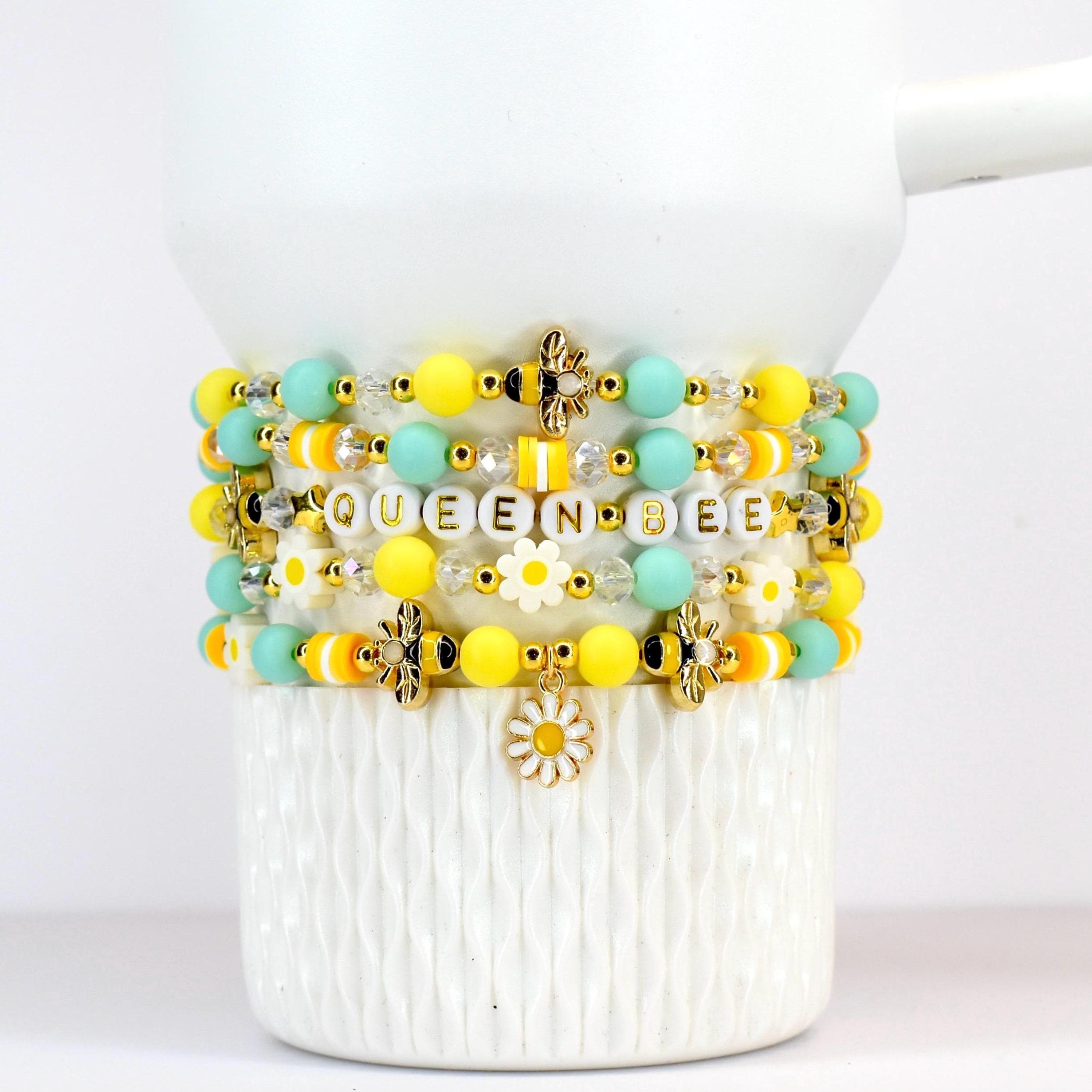 A set of five yellow and mint beaded bracelets with a daisy charm and gold bee beaded accents.