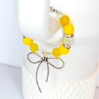A yellow beaded tumbler handle bracelet featuring large yellow beads and clear crystal accents. A silver dragonfly charm hangs from the bracelet. The bracelet is displayed on a white surface.