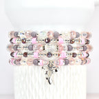 Stack of beaded bracelets in shades of pink, gray, and clear. Each bracelet features a mix of beads, including faceted crystals, round beads, and pink disc beads. A silver bow charm dangles from the bottom bracelet.