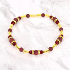 A beaded bracelet featuring a combination of burgundy and gold-colored beads. The bracelet has a repeating pattern of burgundy beads and gold-colored accents, with some sections adorned with small, sparkling embellishments. The bracelet is displayed on a white marble surface.