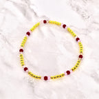 A beaded bracelet featuring small, gold-colored beads interspersed with larger, dark red and light pink beads. The bracelet is circular and likely designed to be worn around the wrist. The beads are strung together, creating a delicate and colorful accessory.