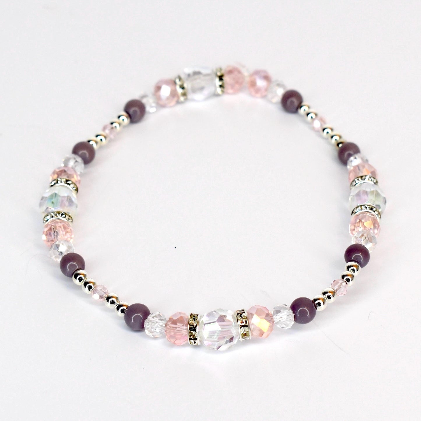 A delicate bracelet featuring a mix of clear, pink, and purple beads. The bracelet includes faceted crystal beads, round purple beads, and small silver-colored spacer beads. The design is strung together, creating a flexible and elegant accessory.