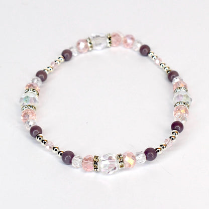 A delicate bracelet featuring a mix of clear, pink, and purple beads. The bracelet includes faceted crystal beads, round purple beads, and small silver-colored spacer beads. The design is strung together, creating a flexible and elegant accessory.