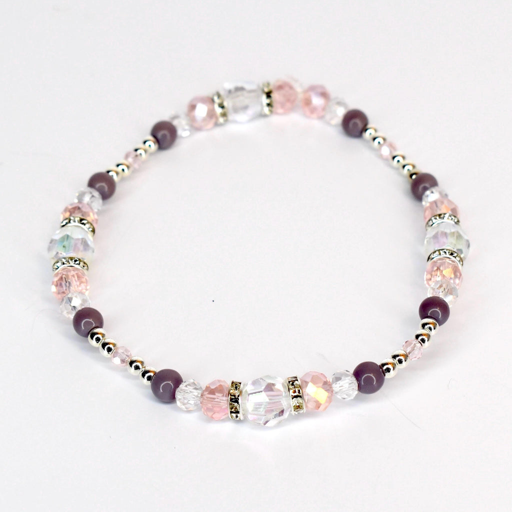 A delicate bracelet featuring a mix of clear, pink, and purple beads. The bracelet includes faceted crystal beads, round purple beads, and small silver-colored spacer beads. The design is strung together, creating a flexible and elegant accessory.